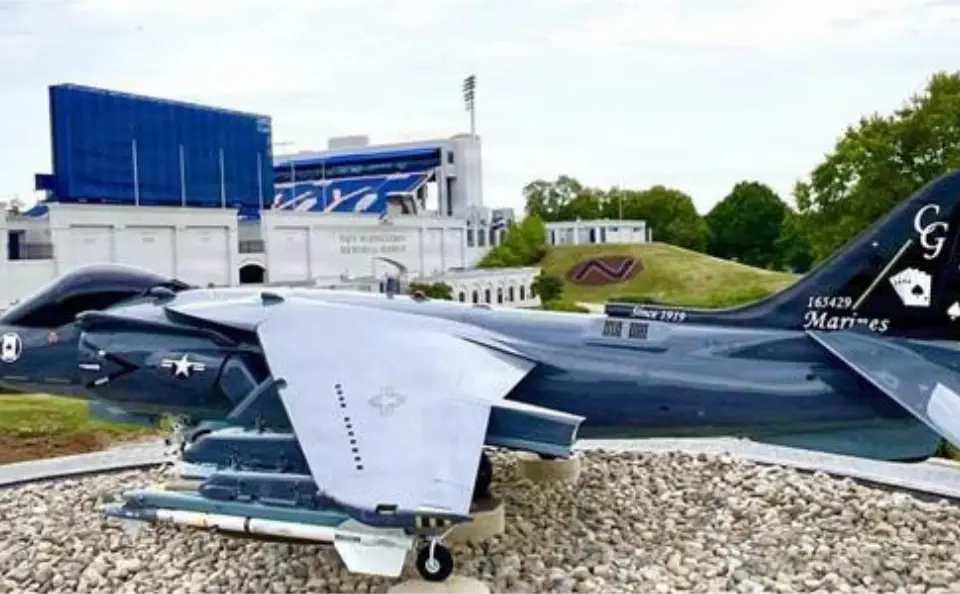 An AV-8B Harrier II on display outdoors with a sports stadium visible in the background.