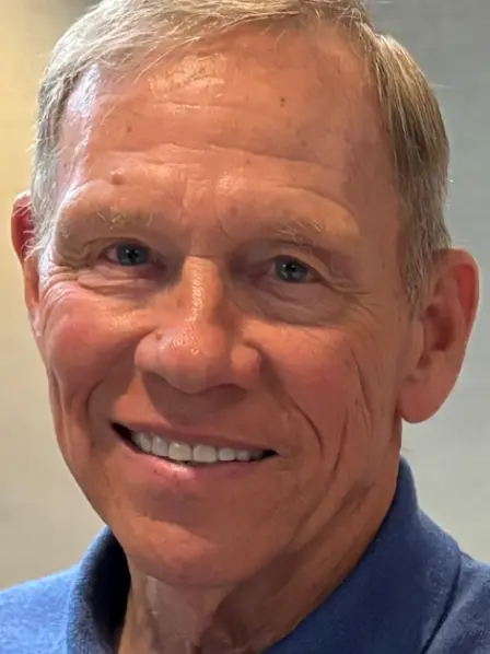 Smiling older man with short light hair, wearing a blue collared shirt, facing the camera.